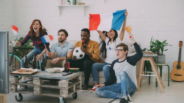 Multi-ethnic group of friends sports fans with French flags watching football championship on TV together at home indoors and cheering up favourite team