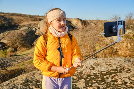Shot of a kid girl talking on camera in hills, make video blog use device make video hold hand social network blog. child vlogger filming video diary outdoors. kid creating social media content.