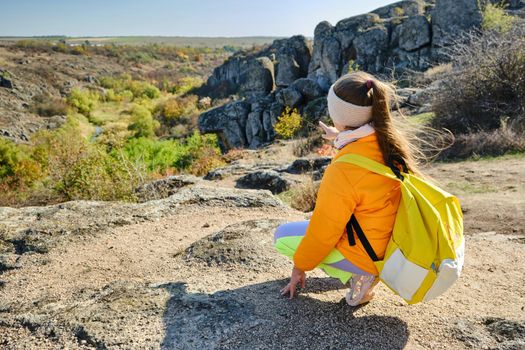 little girl with a yellow backpack standing on a mountain top at the day time