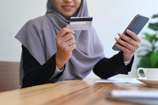 Cropped view of Muslim woman holding credit card and using mobile phone. Online shopping, internet banking concept.