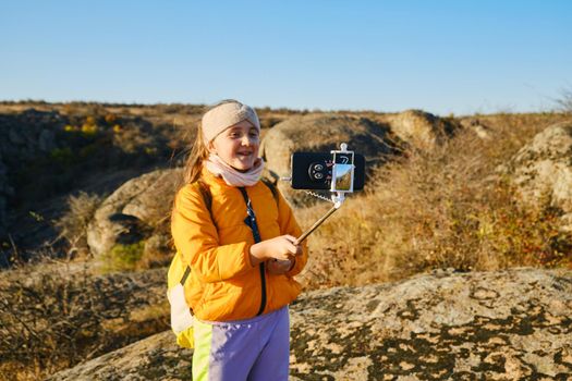 Shot of a kid girl talking on camera in hills, make video blog use device make video hold hand social network blog. child vlogger filming video diary outdoors. kid creating social media content.