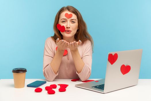 Love you. Amazing woman with kind expression sitting at workplace office, all covered with sticker hearts, sending romantic sensual air kiss, expressing romantic feelings. indoor studio shot isolated