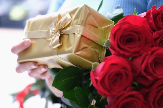 Bouquet of red roses and golden gift box in female hands. Gifts for beloved women concept