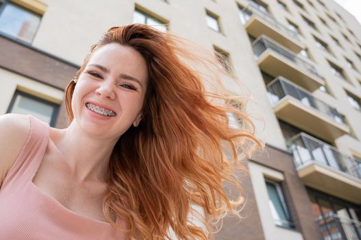 Beautiful young red-haired woman with braces on her teeth smiling in the summer outdoors.