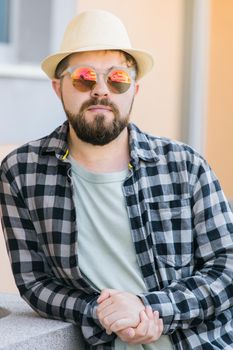 Portrait handsome man wearing summer hat and plaid shirt smiling happy near wall - travel vacations and summer holiday