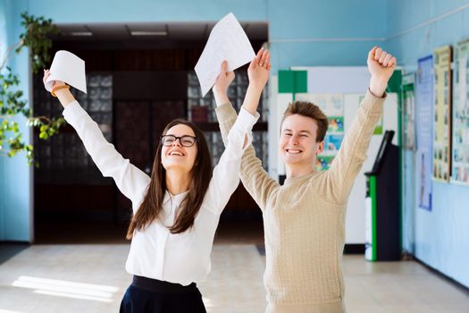 Happy students after researching their checked exams, raising hands up and expressing amusement of getting excellent grades for their work