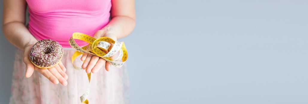 Close-up of woman's hands holding a donut and a measuring tape. The concept of healthy eating. Diet