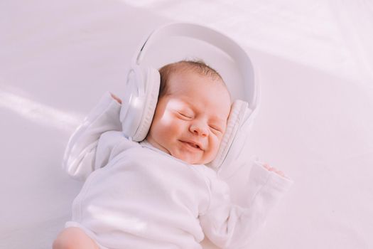 The kid is wearing headphones . Happy baby. A newborn baby. White on white