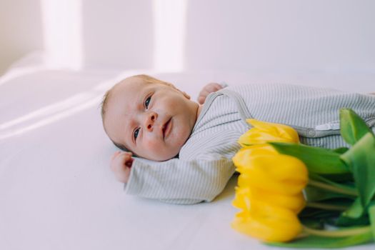 A newborn baby with a bouquet of tulips . A greeting card. March 8th. Baby and flowers. Yellow tulips