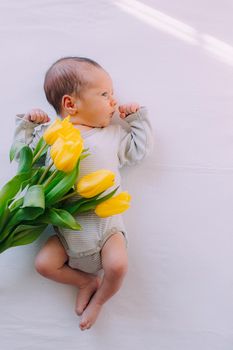 A newborn baby with a bouquet of tulips . A greeting card. March 8th. Baby and flowers. Yellow tulips