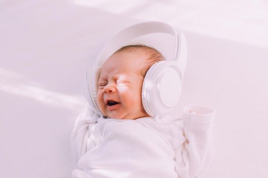 The kid is wearing headphones . Happy baby. A newborn baby. White on white