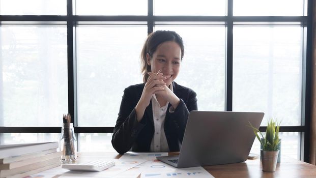 Charming asian businesswoman sitting working on laptop in office..