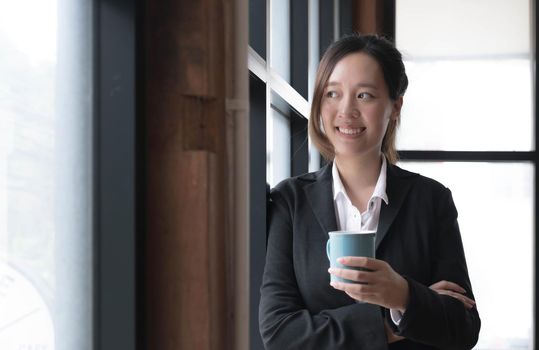 Smiling young Asian businesswoman holding a coffee mug at the office.