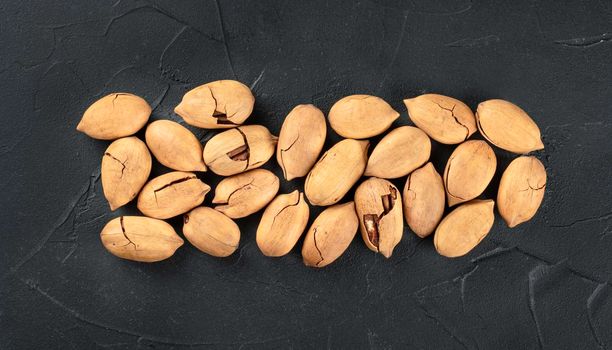 Heap of inshell pecans on dark concrete background, top view