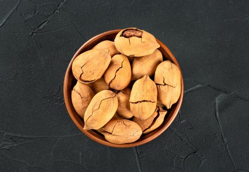 Pecan nuts in a bowl on a dark concrete background, top view.
