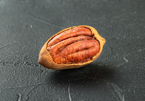 Cracked in-shell pecan close-up on dark concrete background