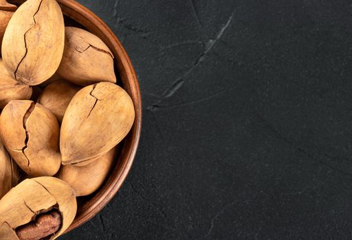 Part of a bowl with in-shell pecans on an empty dark background under the text.