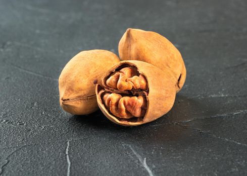 Three shelled pecans nuts close-up on a dark concrete background