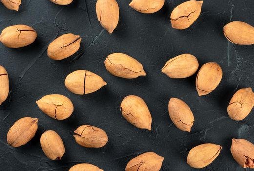 Background of scattered inshell pecans on dark concrete, top view