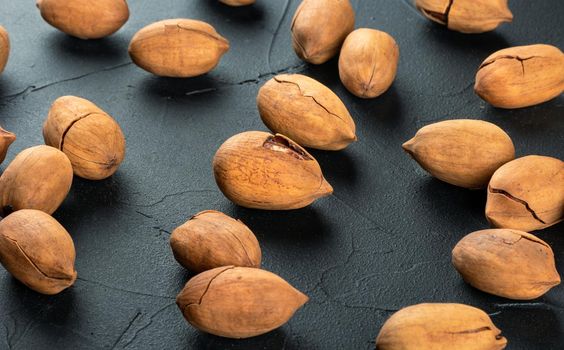 Scattered dry pecans in shell on dark concrete background