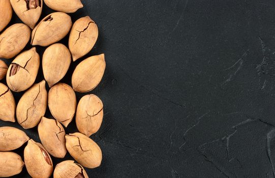 Scattered pecans in shell close up on a dark background, top view