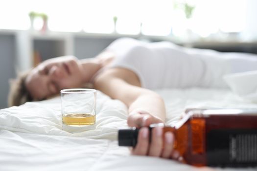 Drunk young woman lies in bed in bottle of alcohol. Female alcoholism and depression concept