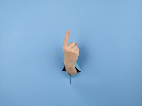 A woman's hand sticking out of a hole from a blue background shows her index finger up