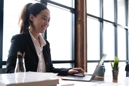 Beautiful young asian woman sitting at coffee shop using laptop. Happy young businesswoman sitting at table in cafe with tab top computer..