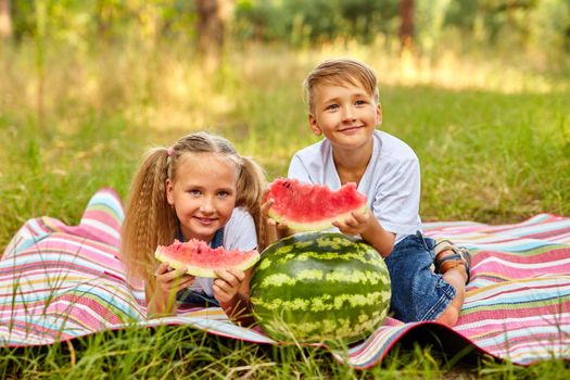 Kids eating watermelon in the park. Kids eat fruit outdoors. Healthy snack for children. Little girl and boy playing in the forest biting a slice of water melon