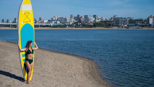 Caucasian woman walks along the beach and carries a sup board on the river in the city. Summer sport