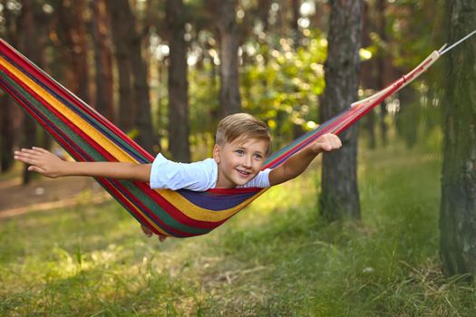 Cute boy is lying in a colorful hammock. The kid is riding in a hammock imagines himself as a flying superhero. Leisure and relax concept