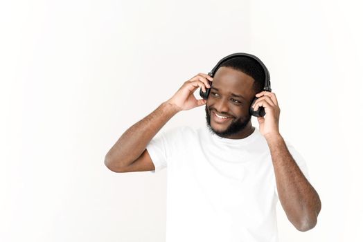 Black young man enjoying music in wireless headphones and singing at white background.