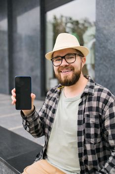 Happy bearded man showing blank smartphone screen over green leaves background - empty space for advertising and copy space.