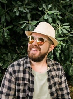 Laughing attractive man wearing hat over green tree background - emotion and vacation travel holidays
