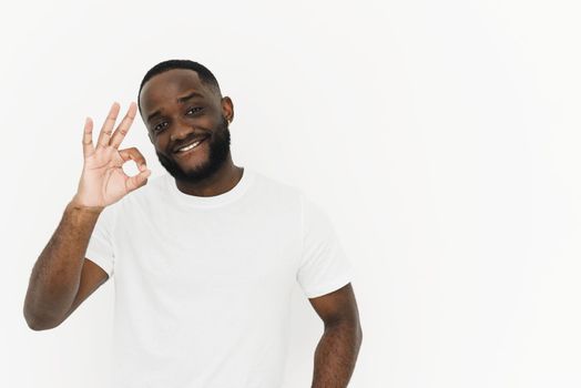 Smiling african american young man in white t-shirt showing ok gesture on white background with copy space.