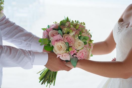 Newlyweds hold hands and a bouquet.