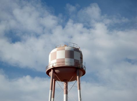 a large Checkered colored water tower against a blue cloudy sky 