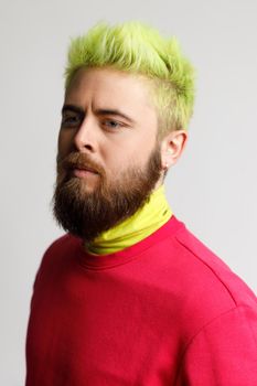 Portrait of serious handsome man with beard and yellow hair, wearing casual red jumper, looking focused at camera, has confident expression. Indoor studio shot isolated on gray background.