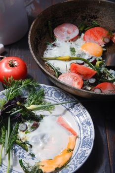 Fried eggs with young garlic stems, greenery, basil and tomatoes on frying pan and on plate. selective focus, top view.