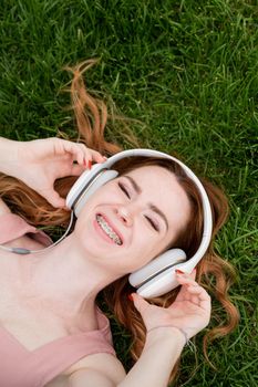 A young red-haired woman lies on the grass and listens to music