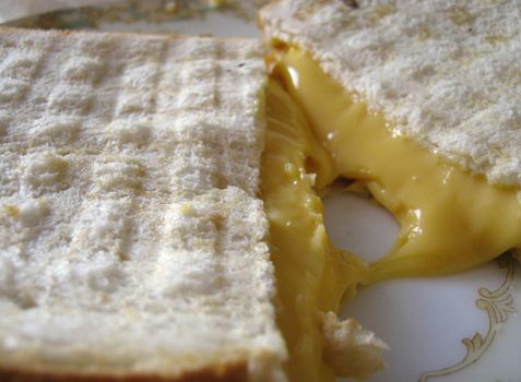 A closeup of a melting grilled cheese sandwich on white bread, with grill marks.  On a fancy plate.