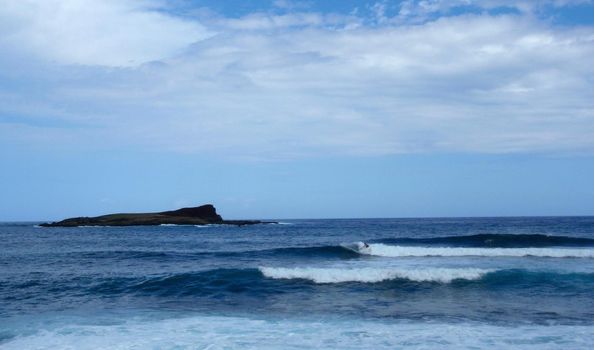 Man Surfs in front of Kaohikaipu (Black Rock) Island on a beautiful day.  Oahu, Hawaii
