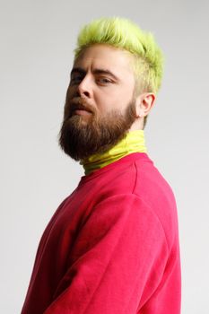 Portrait of proud handsome young bearded Caucasian man in red casual sweater, looking with prideful face,standing half sideways smug puffed. Indoor studio shot isolated on gray background.