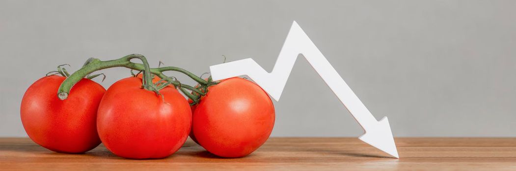 The price of tomatoes and vegetables. Bad vegetable harvest. Fresh red ripe tomatoes with twigs on the table. Graph chart points down