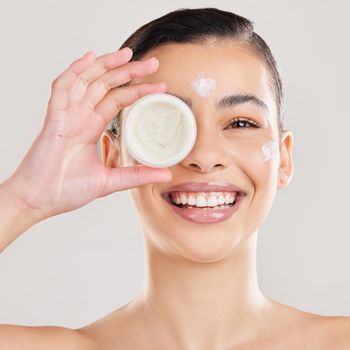 Shot of a young woman applying a cream to her face against a grey background.