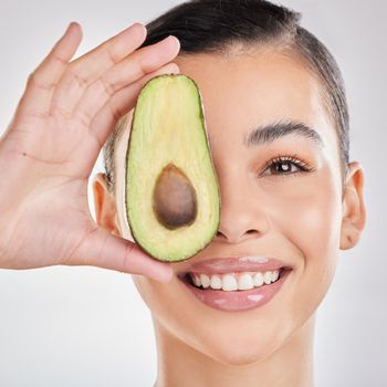 Studio shot of a young woman posing with half an avocado against a grey background.