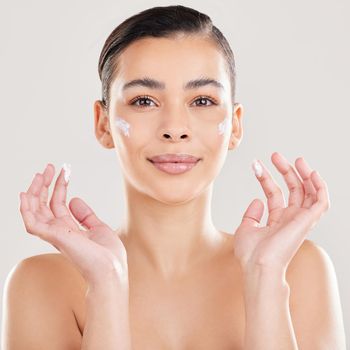 Shot of a young woman applying a cream to her face against a grey background.