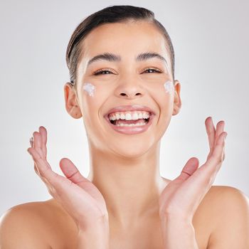 Shot of a young woman applying a cream to her face against a grey background.