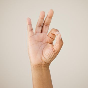 Cropped shot of a man showing a hand sign against a studio background.