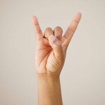 Cropped shot of a man showing a hand sign against a studio background.